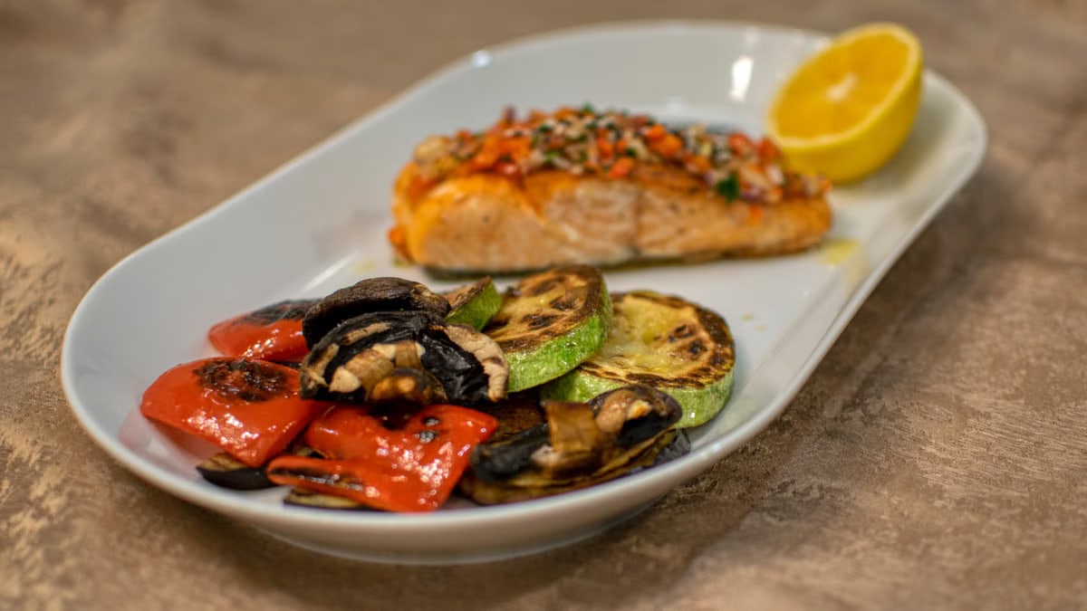 A delicious grilled salmon fillet with roasted vegetables served on a white plate.